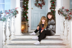 Mom and daughter in cozy home, decorated entrance to house with bright colours. Family waiting for New year. Family photo session in Christmas interiors